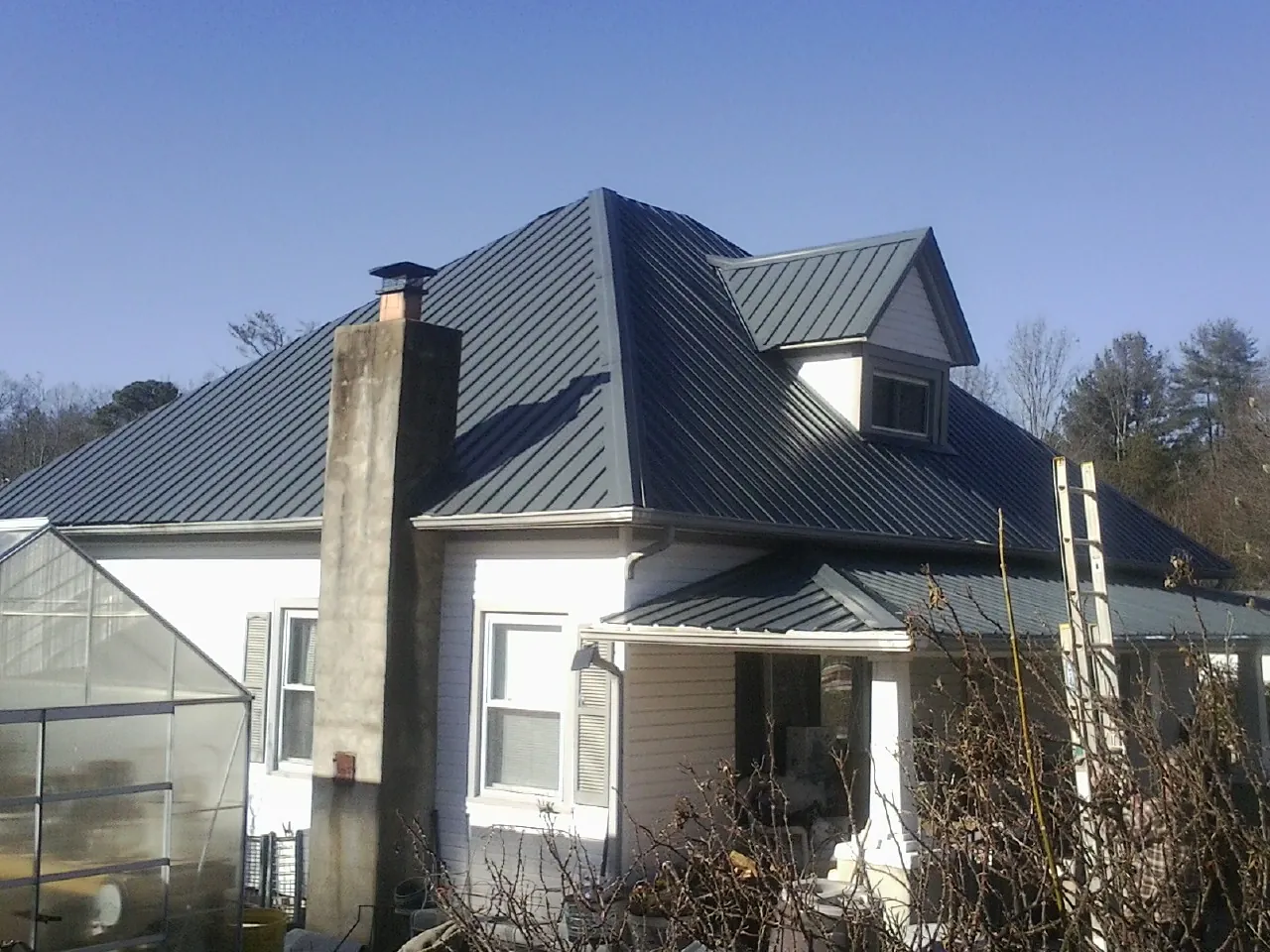 Dark blue standing seam metal roof on a white farmhouse with dormer — Slate & Tile Roof Repair by Roofing Brothers in Keithsburg