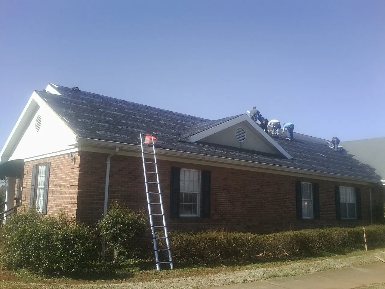 Crew tearing shingles off a brick ranch roof with a ladder set — Emergency Roof Repair work by our crew in Keithsburg