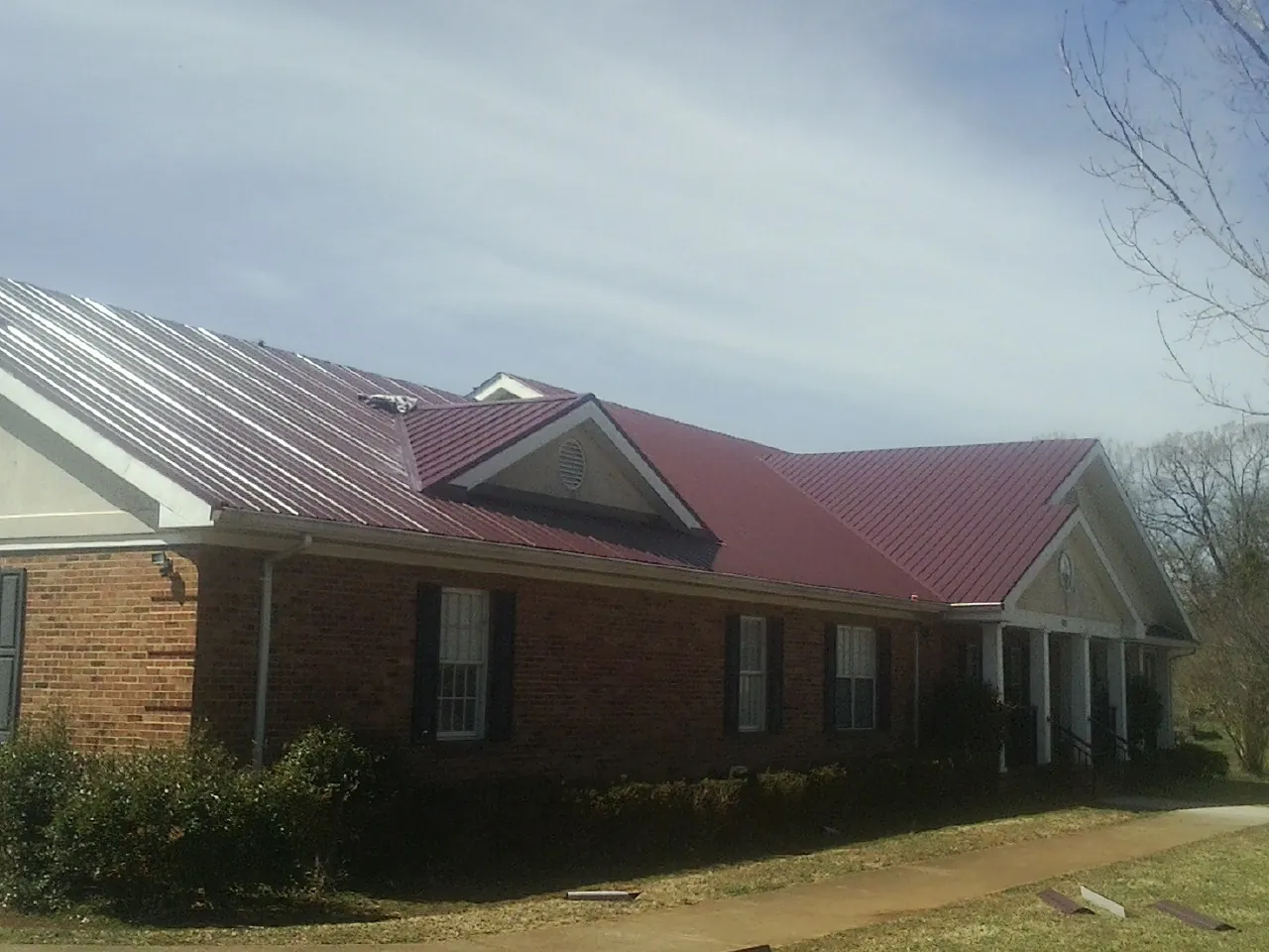 Red metal roof with gabled entries on a long brick building, from a Hail Damage Roof Repair job in Keithsburg