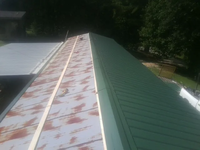 Old rusted panels beside newly installed green metal roofing — Wind Damage Roof Repair by Roofing Brothers in Keithsburg