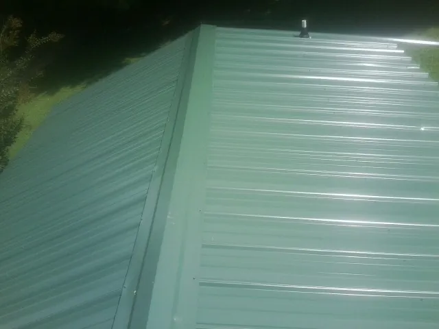 New green metal panels meeting at the ridge of a roof — Flat Roof Repair work by our crew in Keithsburg