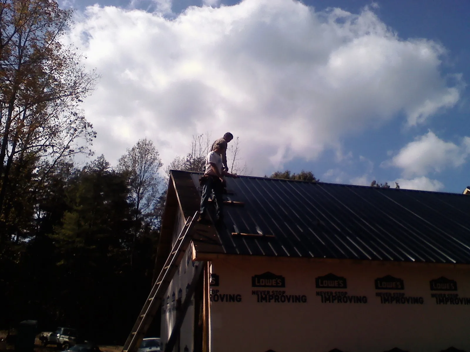 Roofer fastening dark metal panels high against a cloudy sky, from a Roof Inspection job in Keithsburg